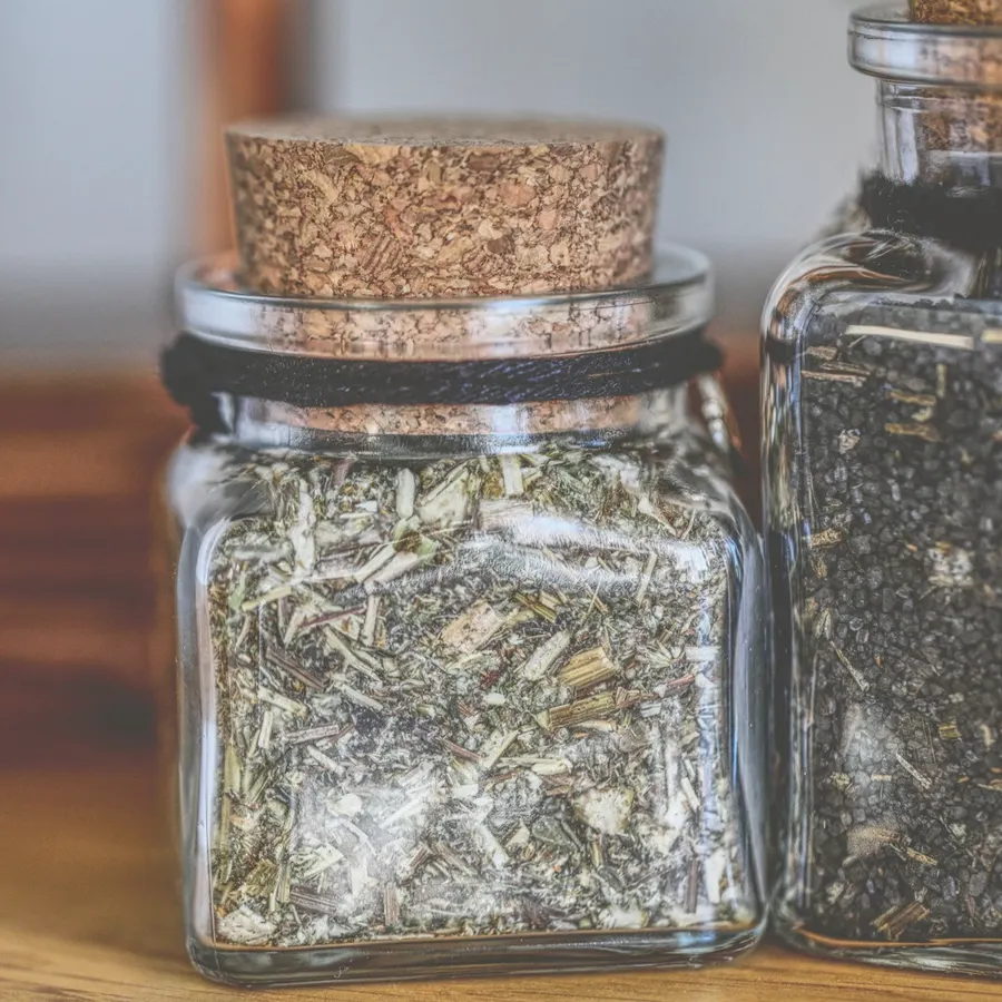 Cork-stoppered glass jar of dried chopped herbs on a wooden table