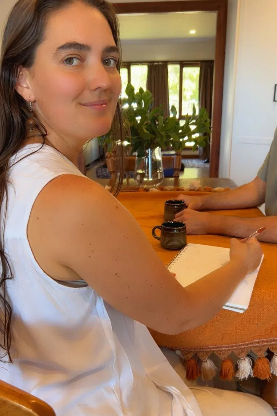 Stefanie, naturopath, smiling at a dining table during a consultation, notebook and pen in hand