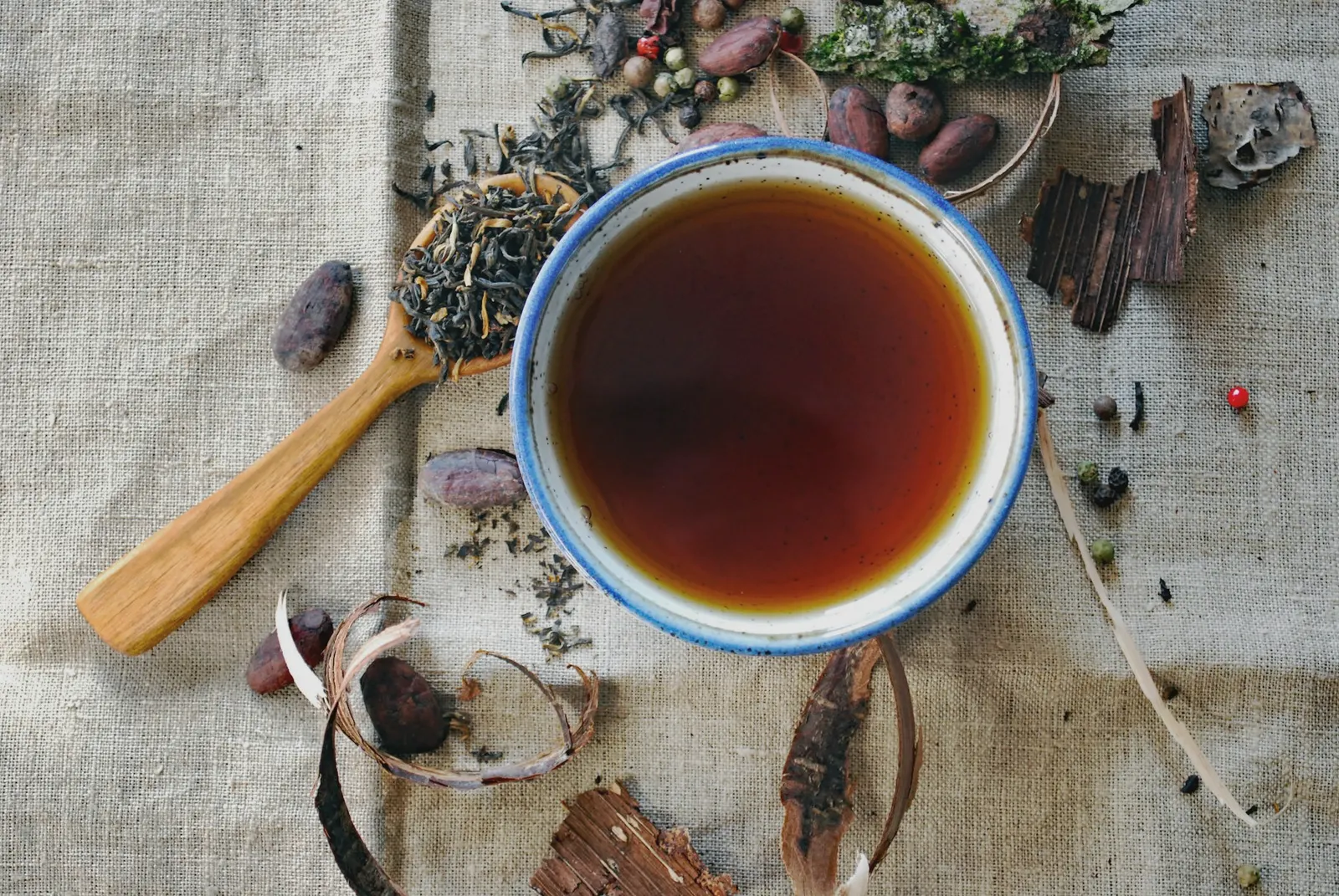 Herbal tea in a ceramic cup on linen, with loose leaf tea on a wooden spoon