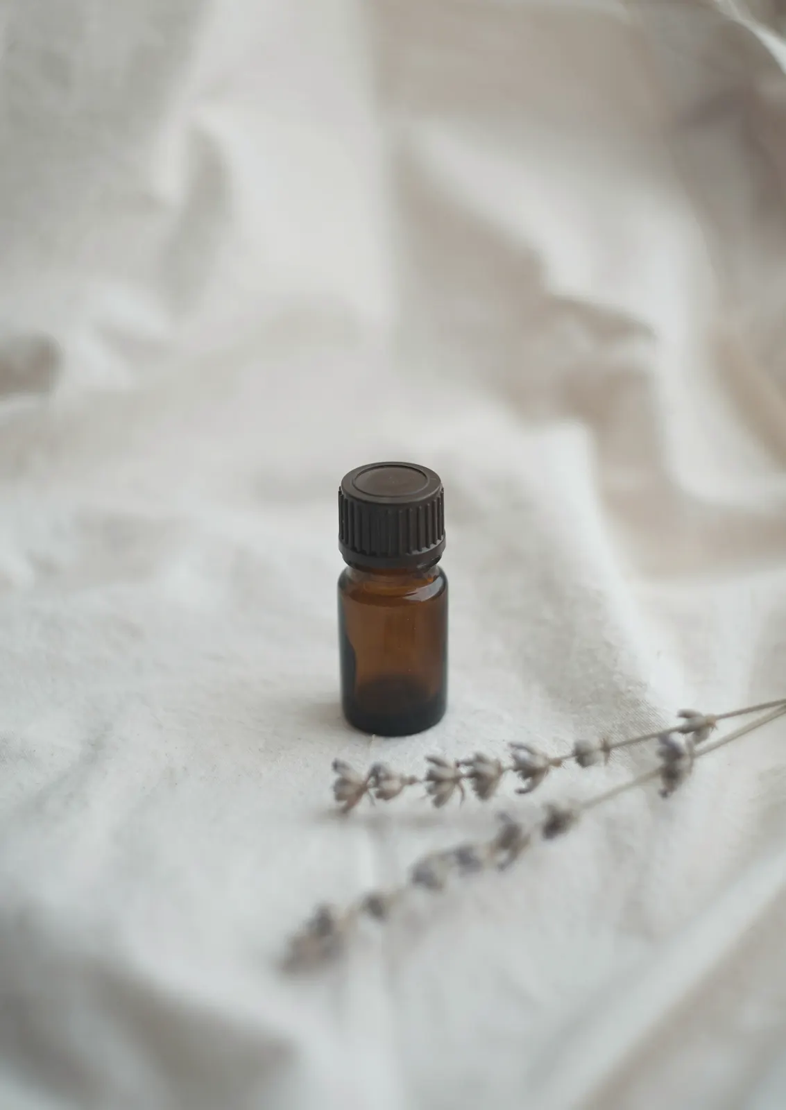 Small amber glass bottle on cream linen beside sprigs of dried lavender
